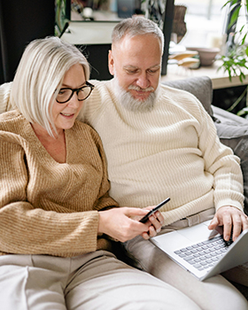 älteres Pärchen auf Couch mit Smartphone und Laptop